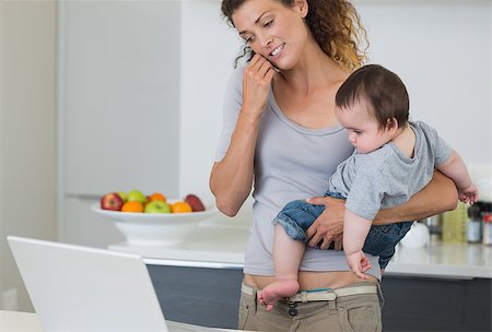 Mother answering cellphone while carrying baby boy in kitchen Stock Photo - Budget Royalty-Free & Subscription, Code: 400-07335662
