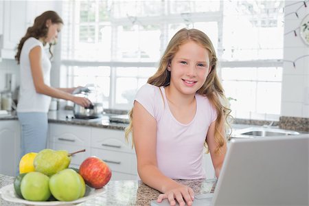 Portrait of a daughter using laptop with mother cooking food in background at the kitchen Stock Photo - Budget Royalty-Free & Subscription, Code: 400-07339682