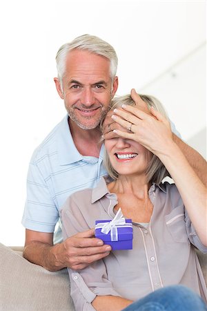 simsearch:6109-07601570,k - Portrait of a smiling mature man surprising woman with a gift on sofa at home Stockbilder - Microstock & Abonnement, Bildnummer: 400-07333878