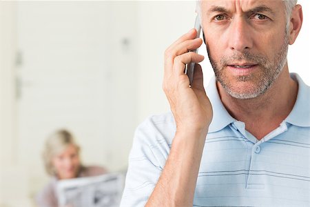 Closeup of a mature man using cellphone with woman reading newspaper in background at home Stock Photo - Budget Royalty-Free & Subscription, Code: 400-07333961