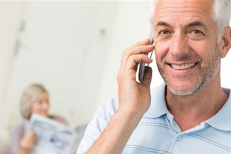 Closeup of a mature man using cellphone with woman reading newspaper in background at home Stock Photo - Budget Royalty-Free & Subscription, Code: 400-07333962