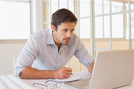simsearch:614-02003461,k - Concentrated young businessman working on blueprints and laptop in the office Stock Photo - Budget Royalty-Free & Subscription, Code: 400-07340894