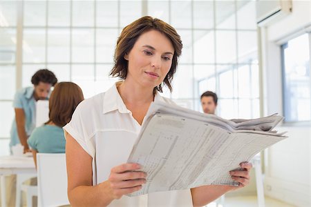 Young businesswoman reading newspaper with colleagues in meeting in background at the office Stock Photo - Budget Royalty-Free & Subscription, Code: 400-07341471