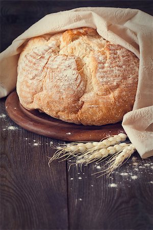 Fresh bread with wheat ears and rustic kitchen towel on a wooden cutting board. Toned photo. Stock Photo - Budget Royalty-Free & Subscription, Code: 400-07414879