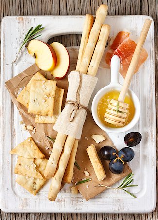 simsearch:400-08070576,k - Grissini bread sticks, crackers with salt, rosemary honey, prosciutto ham, apple and grape on a white cooking board. Foto de stock - Super Valor sin royalties y Suscripción, Código: 400-07414885