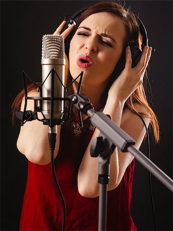 Photo of a beautiful woman singing into a large diaphragm microphone over dark background. Stock Photo - Budget Royalty-Free & Subscription, Code: 400-07416147