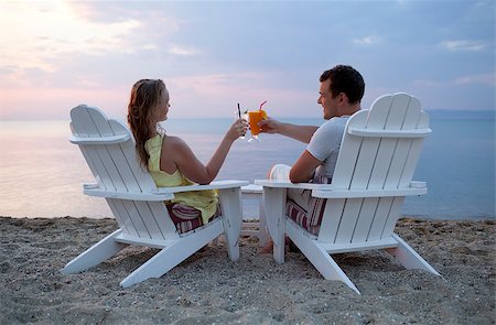 Romantic couple sitting in wooden deckchairs on the beach toasting the sunset clinking their cocktail glasses together, view from behind looking out to sea Stock Photo - Budget Royalty-Free & Subscription, Code: 400-07418726