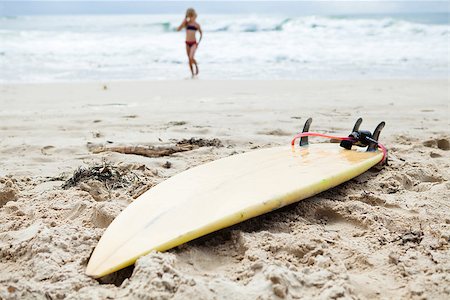 Closeup of surfboard lying in sand on beach with young girl standing in water in the background Photographie de stock - Aubaine LD & Abonnement, Code: 400-07420203