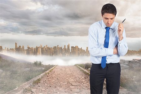 simsearch:400-07446838,k - Thinking businessman holding pen against stony path leading to large urban sprawl Photographie de stock - Aubaine LD & Abonnement, Code: 400-07446874