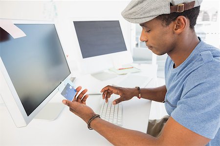 simsearch:400-07333971,k - Side view of a casual young man doing online shopping through computer and credit card in office Stock Photo - Budget Royalty-Free & Subscription, Code: 400-07466590