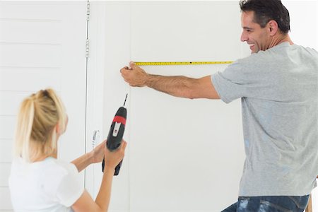 Rear view of a woman holding drill while man measuring the wall at new home Stock Photo - Budget Royalty-Free & Subscription, Code: 400-07467906