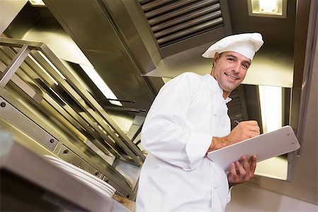 simsearch:400-07468062,k - Low angle portrait of a smiling male cook writing on clipboard in the kitchen Stockbilder - Microstock & Abonnement, Bildnummer: 400-07468065