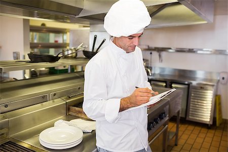 simsearch:400-07468062,k - Side view of a concentrated male cook writing on clipboard in the kitchen Stockbilder - Microstock & Abonnement, Bildnummer: 400-07468068