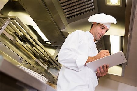 simsearch:400-07468062,k - Low angle view of a concentrated male cook writing on clipboard in the kitchen Stockbilder - Microstock & Abonnement, Bildnummer: 400-07468063