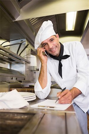Portrait of a smiling male cook writing on clipboard while using cellphone in the kitchen Photographie de stock - Aubaine LD & Abonnement, Code: 400-07468074