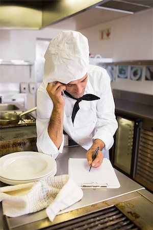 Concentrated male cook writing on clipboard while using cellphone in the kitchen Photographie de stock - Aubaine LD & Abonnement, Code: 400-07468075