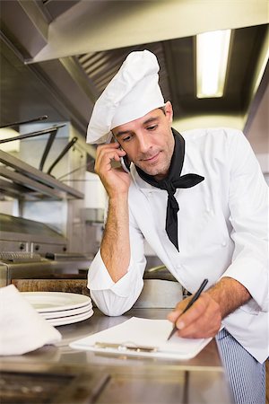 simsearch:400-07468062,k - Concentrated male cook writing on clipboard while using cellphone in the kitchen Stockbilder - Microstock & Abonnement, Bildnummer: 400-07468071