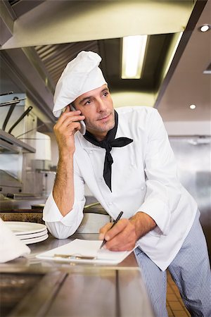 simsearch:400-07468062,k - Concentrated male cook writing on clipboard while using cellphone in the kitchen Stockbilder - Microstock & Abonnement, Bildnummer: 400-07468072