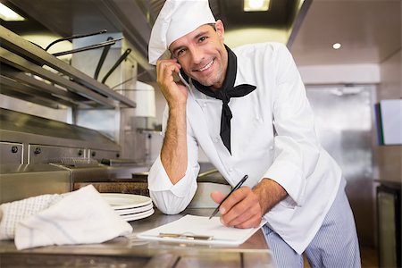 simsearch:400-07468062,k - Portrait of a smiling male cook writing on clipboard while using cellphone in the kitchen Stockbilder - Microstock & Abonnement, Bildnummer: 400-07468073