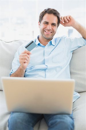 simsearch:400-07474252,k - Cheerful man using laptop sitting on sofa shopping online at home in the living room Stock Photo - Budget Royalty-Free & Subscription, Code: 400-07474244
