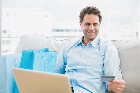 simsearch:400-07474252,k - Handsome man using laptop sitting on sofa shopping online at home in the living room Stock Photo - Budget Royalty-Free & Subscription, Code: 400-07474245
