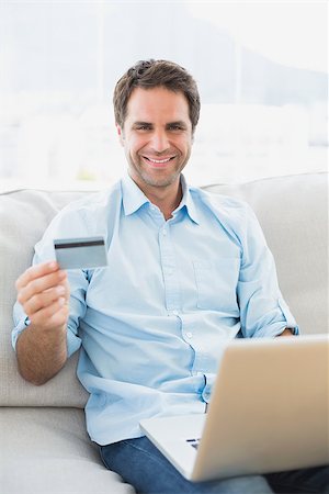simsearch:400-07474252,k - Smiling man using laptop sitting on sofa shopping online at home in the living room Stock Photo - Budget Royalty-Free & Subscription, Code: 400-07474242