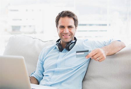 simsearch:400-07474252,k - Happy handsome man sitting on sofa online shopping with laptop at home in the living room Stock Photo - Budget Royalty-Free & Subscription, Code: 400-07474252