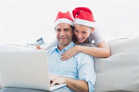 simsearch:400-07474252,k - Smiling couple in santa hats shopping online with laptop at home in the living room Stock Photo - Budget Royalty-Free & Subscription, Code: 400-07474268