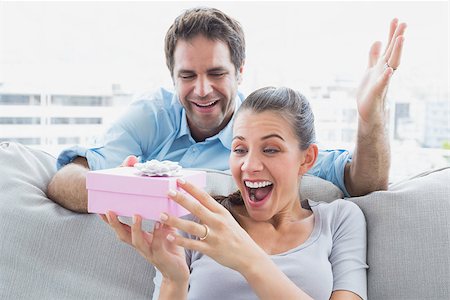simsearch:6109-07601570,k - Man surprising his pretty girlfriend with a pink gift on the sofa at home in the living room Stockbilder - Microstock & Abonnement, Bildnummer: 400-07474292