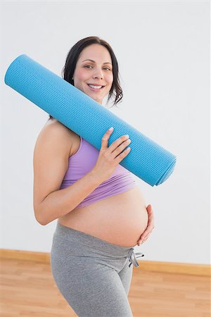 simsearch:400-06690931,k - Pregnant woman holding exercise mat smiling at camera in a fitness studio Fotografie stock - Microstock e Abbonamento, Codice: 400-07474419