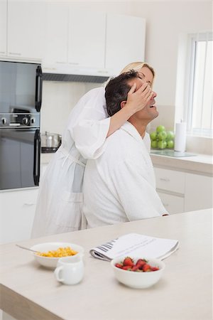 Side view of a woman covering man's eyes at breakfast table in the kitchen at home Foto de stock - Super Valor sin royalties y Suscripción, Código: 400-07475255