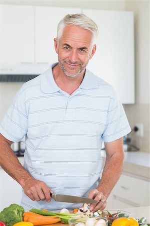 simsearch:400-06874653,k - Casual man slicing vegetables and smiling at camera at home in the kitchen Photographie de stock - Aubaine LD & Abonnement, Code: 400-07475827