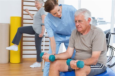 simsearch:400-07335332,k - Female therapist assisting senior man with dumbbells in the medical office Fotografie stock - Microstock e Abbonamento, Codice: 400-07476640