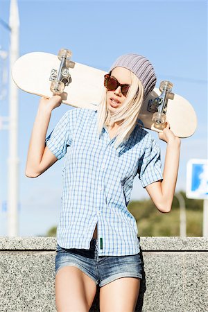 Close-up of young blond girl in beanie hat and leopard sunglasses who stands near granite fence on sunny day holding skateboard on her shoulders Stock Photo - Budget Royalty-Free & Subscription, Code: 400-07477501
