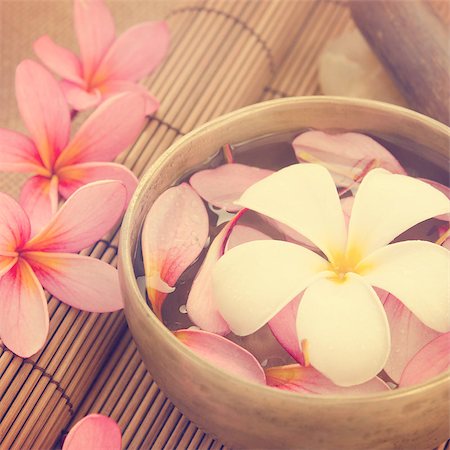 Spa setting, low light with ambient in vintage revival tone. Frangipani, hot and cold stone on bamboo mat. Foto de stock - Super Valor sin royalties y Suscripción, Código: 400-07470843