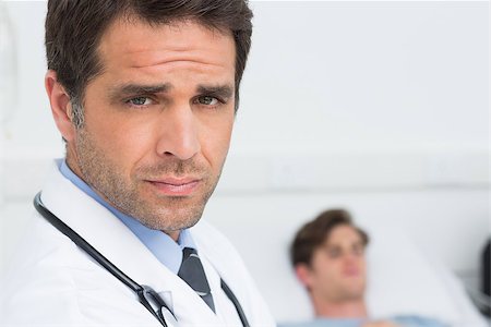 simsearch:400-07334526,k - Portrait of confident male doctor with male patient in background at hospital ward Foto de stock - Super Valor sin royalties y Suscripción, Código: 400-07473415