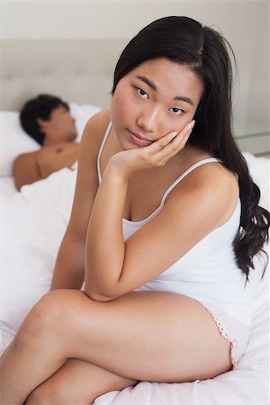 Woman sitting on end of bed as boyfriend sleeps at home in bedroom Stock Photo - Budget Royalty-Free & Subscription, Code: 400-07483070