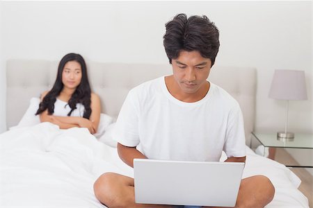 Woman watching boyfriend using laptop on end of bed at home in bedroom Stock Photo - Budget Royalty-Free & Subscription, Code: 400-07483084