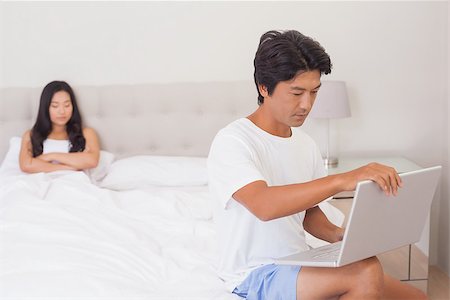 Woman watching boyfriend using laptop on end of bed at home in bedroom Stock Photo - Budget Royalty-Free & Subscription, Code: 400-07483088