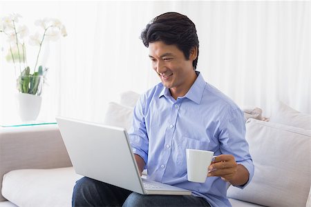 simsearch:400-07474252,k - Happy man sitting on couch using laptop having coffee at home in the living room Stock Photo - Budget Royalty-Free & Subscription, Code: 400-07483241