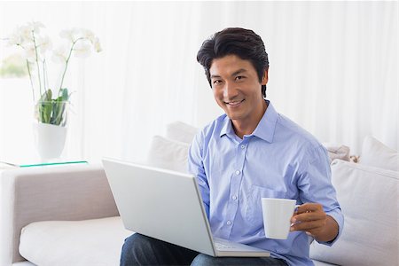 simsearch:400-07474252,k - Happy man sitting on couch using laptop having coffee at home in the living room Stock Photo - Budget Royalty-Free & Subscription, Code: 400-07483242