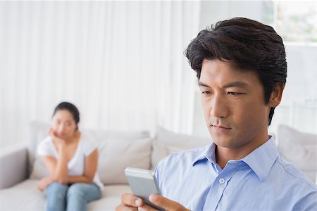 simsearch:400-07483384,k - Man sending a text while girlfriend watches from couch at home in the living room Stock Photo - Budget Royalty-Free & Subscription, Code: 400-07483278