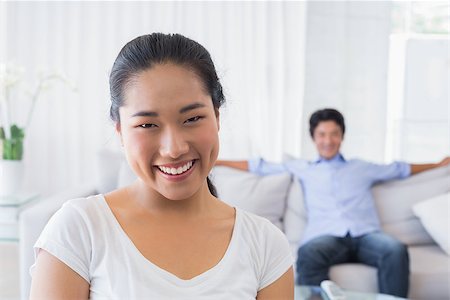 simsearch:400-07483384,k - Happy woman smiling at camera with boyfriend in back at home in the living room Stock Photo - Budget Royalty-Free & Subscription, Code: 400-07483273