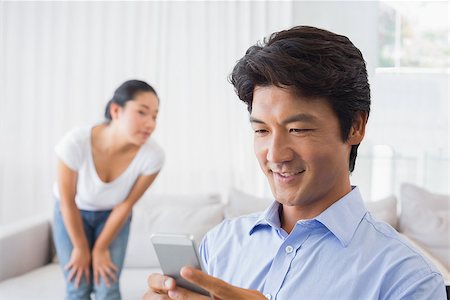 simsearch:400-07483384,k - Man sending a text while girlfriend watches from couch at home in the living room Stock Photo - Budget Royalty-Free & Subscription, Code: 400-07483280