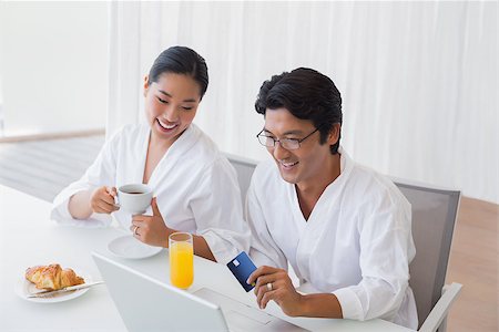 simsearch:400-07483384,k - Couple in bathrobes shopping online in the morning at home in the living room Stock Photo - Budget Royalty-Free & Subscription, Code: 400-07483383