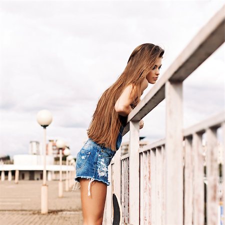 young beautiful girl with long legs and silky hair in denim short overalls stands on tiptoes hanging over bridge Stock Photo - Budget Royalty-Free & Subscription, Code: 400-07506251
