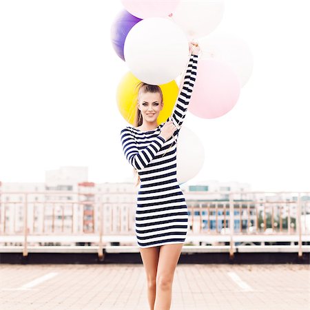 simsearch:400-07506274,k - beautiful girl with ponytail hair in short black and white striped dress and white high sneakers walks forward holding bunch of multicolored balloons Fotografie stock - Microstock e Abbonamento, Codice: 400-07506263