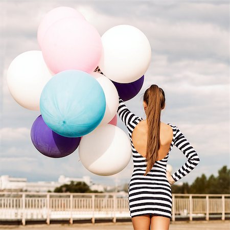 simsearch:400-07506274,k - back view of girl in open-back black and white striped short dress and white high top sneakers holds a bunch of multicolored balloons Fotografie stock - Microstock e Abbonamento, Codice: 400-07506275