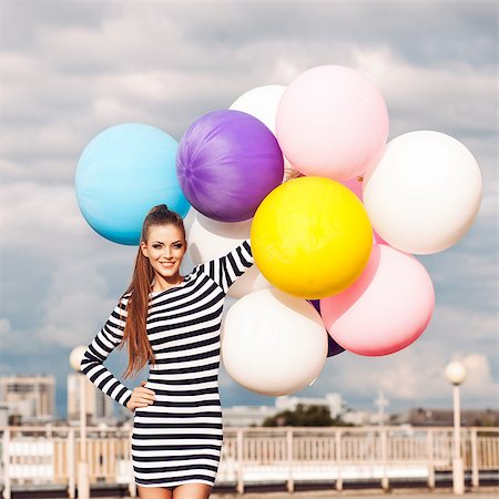 beautiful young lady in black and white striped short dress holds a bunch of multicolored balloons smiling for camera Stock Photo - Budget Royalty-Free & Subscription, Code: 400-07506273
