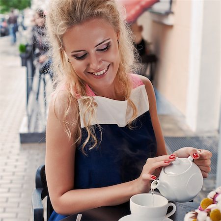 a beautiful young blond girl with a happy toothy smile in summer dress at the table in pavement cafe is pouring green tea from the teapot into a white ceramic cup Stock Photo - Budget Royalty-Free & Subscription, Code: 400-07509914